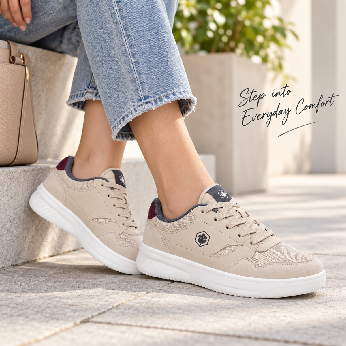 A person wearing beige low-top sneakers with white soles, shown from the knees down while sitting on stone steps outdoors. Light blue jeans are visible, along with a beige handbag and a blurred plant in the background.